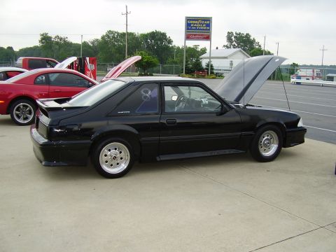 1988 Ford Mustang - A black 1988 Ford Mustang coupe is parked with its hood open, alongside a red car.
