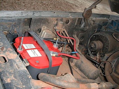 1980 Ford Bronco - The engine bay shows a red battery secured with a strap, surrounded by various hoses and wiring.