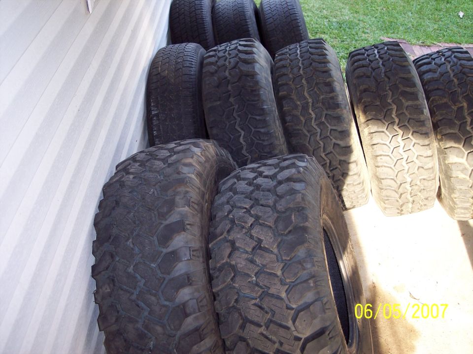 Stack of off-road tires leaning against a wall and on the ground