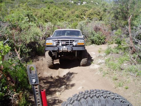 1994 Ford Bronco - A black Ford Bronco navigates a rocky, off-road trail with a modified bumper and large tires.