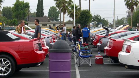 1990 Ford Probe - Multiple Ford Mustangs are parked in a lot, with people milling around them.