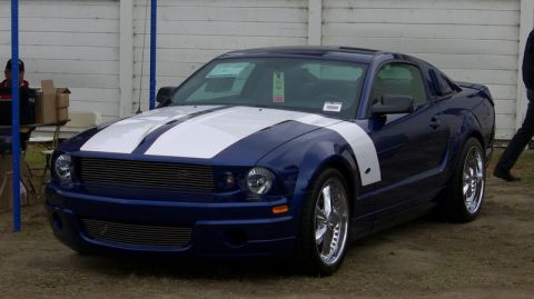 1990 Ford Probe - A blue Ford Mustang with white racing stripes is parked outdoors, with a white fence in the background.
