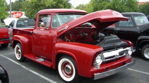 1990 Ford Probe - Red 1950s Ford pickup truck with its hood open, parked alongside another truck.