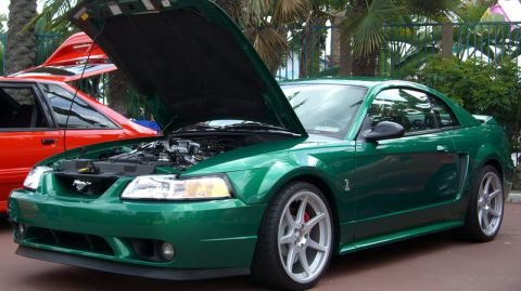 1990 Ford Probe - Green coupe with hood open, revealing the engine and prominent red brake calipers on the front wheel.