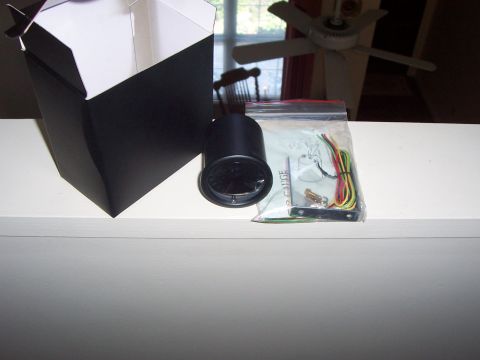 1993 Ford Probe - A black gauge, its wiring harness, and an open black and white box are displayed on a white surface.