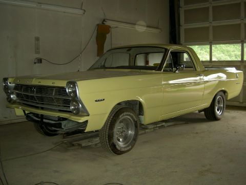1967 Ford Ranchero - A yellow 1967 Ford Ranchero pickup truck is parked in a garage, showing its front end and side profile.