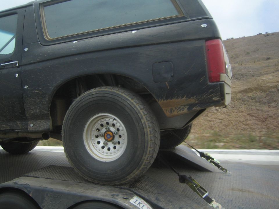 Rear quarter of a black SUV on a trailer showing a white alloy wheel