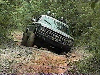 1980 Ford Bronco - A four-wheel-drive vehicle navigates a challenging off-road trail surrounded by dense foliage.
