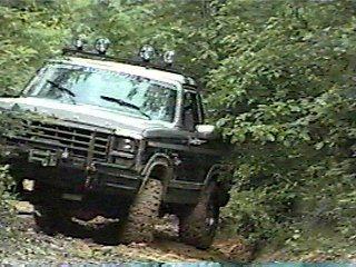 1980 Ford Bronco - This Ford Bronco is navigating a wooded trail with muddy tires and extra lights on its roof.