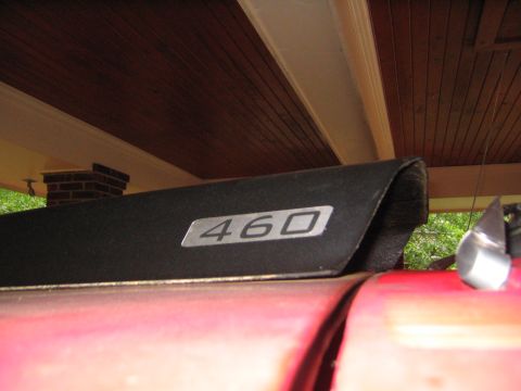 1979 Ford Bronco - Low-angle close-up of a silver "460" engine-displacement badge on the black hood scoop or hood edge of a red truck parked under a wood-ceil…