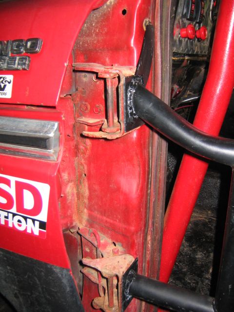1979 Ford Bronco - Close-up of a red early Ford Bronco's door opening with the factory door removed, exposing surface-rusted body-side hinges and a black tubu…