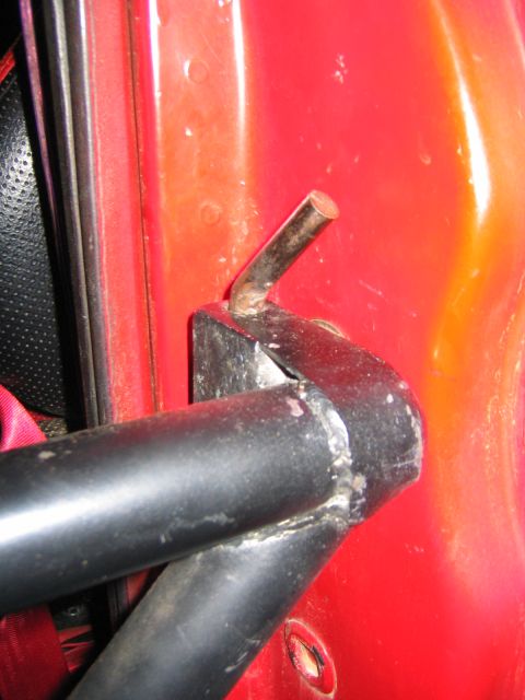 1979 Ford Bronco - Detail of a homemade black tube door frame welded to a bracket at the front edge of a red door skin, with a bare steel hinge or latch pin p…