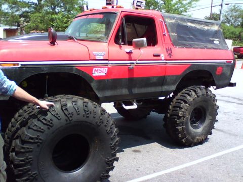 1979 Ford Bronco - Red and black lifted Ford Bronco on massive mud tires parked in a lot, MSD and Bronco decals visible.