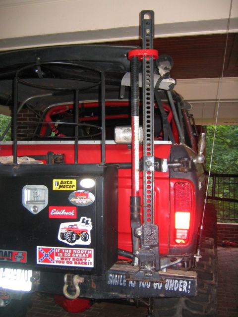 1979 Ford Bronco - Rear corner view of a red off-road SUV parked under a carport, showing a black rear tailgate panel covered in Auto Meter, Holley, Edelbrock…
