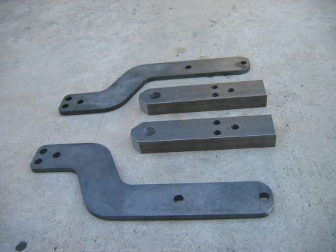 1985 Toyota 4Runner - Metal brackets with various hole patterns are laid out on a concrete surface, suggesting automotive parts.
