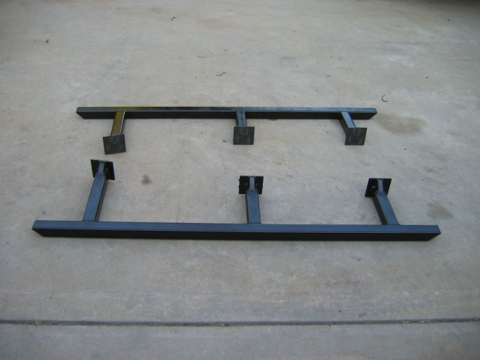 Two black metal running boards with square mounting brackets on a concrete surface