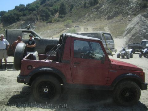 1987 Suzuki Samurai - A red 1987 Suzuki Samurai is seen off-roading with other vehicles in the background.