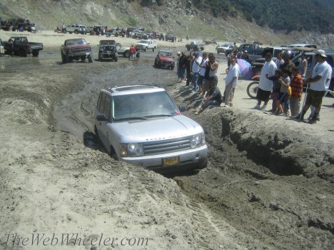 1987 Suzuki Samurai - Off-roading event shows a Range Rover struggling in thick mud, surrounded by onlookers and other vehicles.