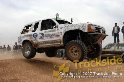 1992 Ford Explorer - Modified SUV jumps during an off-road race, with spectators watching from the sidelines.