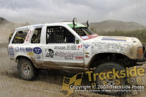 1992 Ford Explorer - A white 1992 Ford Explorer competes in an off-road race, covered in mud and adorned with numerous sponsor decals.