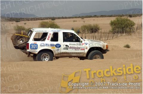 1992 Ford Explorer - Off-road race vehicle navigates sandy terrain, displaying various sponsor decals and the number 301.