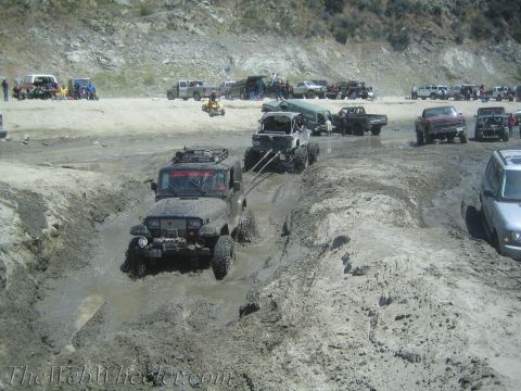 1987 Suzuki Samurai - Off-road vehicles tackle a challenging muddy course, with multiple vehicles and people present.