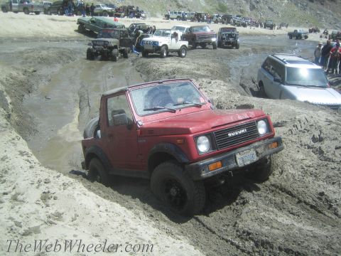 1987 Suzuki Samurai - Multiple vehicles are seen off-roading in a muddy terrain, with a red Suzuki Samurai prominently featured.