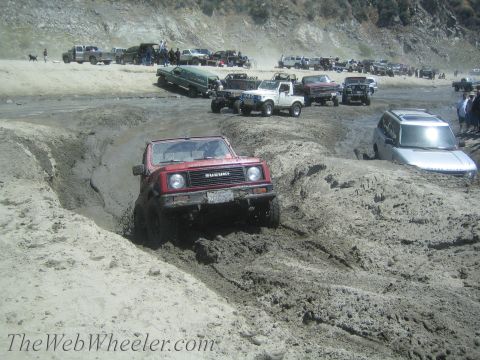 1987 Suzuki Samurai - Red 1987 Suzuki Samurai tackling a challenging muddy trail alongside other off-road vehicles.