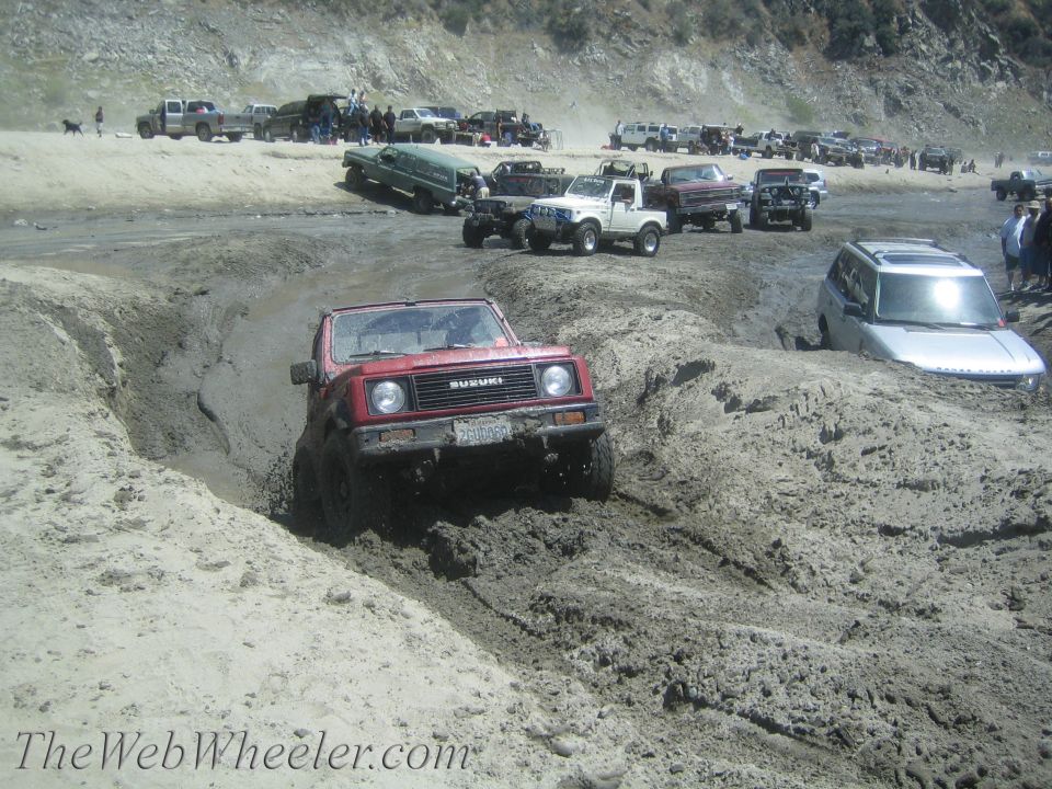 Red 1987 Suzuki Samurai navigating a muddy off-road course with other vehicles in the background