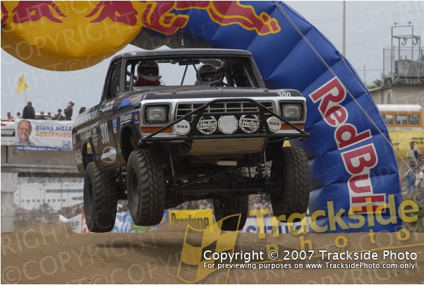 Pickup truck with roll cage and off-road tires mid-air jump, Red Bull arch in background