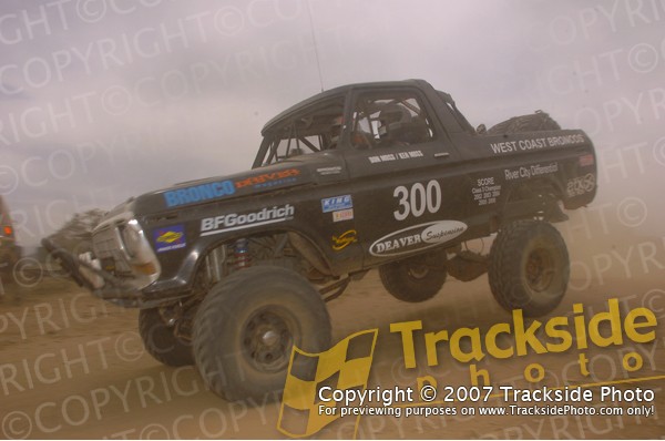 Black off-road race truck with number 300, modified body, large tires, and roll cage, kicking up dust