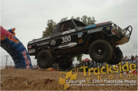 1992 Ford Explorer - A modified Ford Bronco jumps over a dirt ramp during a race, with spectators in the background.