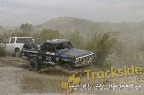 1992 Ford Explorer - A black pickup truck navigates a muddy track, followed by a white SUV, during an off-road event.