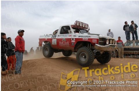 1992 Ford Explorer - A custom off-road truck competes in a race, kicking up dust as it jumps over a mound.