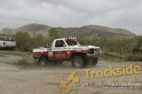 1992 Ford Explorer - A red and white off-road race truck navigates a muddy track, with another vehicle visible in the background.