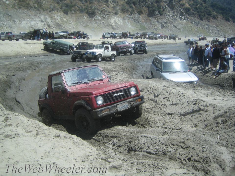 Red 1987 Suzuki Samurai navigating a muddy off-road course