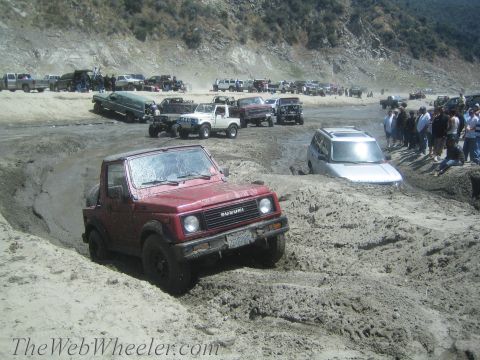 1987 Suzuki Samurai - Red 1987 Suzuki Samurai navigating a mud pit with spectators and other vehicles present.
