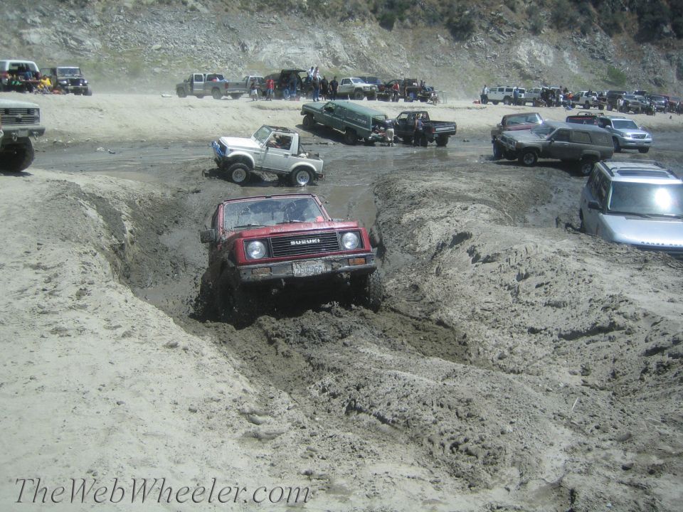 Red 1987 Suzuki Samurai navigating a muddy off-road course