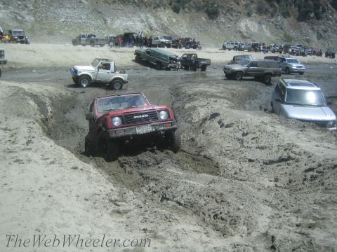 1987 Suzuki Samurai - Red 1987 Suzuki Samurai tackling a challenging muddy terrain alongside other off-road vehicles.