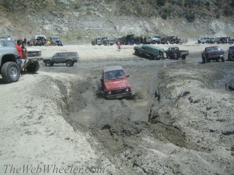 1987 Suzuki Samurai - A group of off-road vehicles gathered at a muddy terrain, with one vehicle stuck in a deep mud pit.