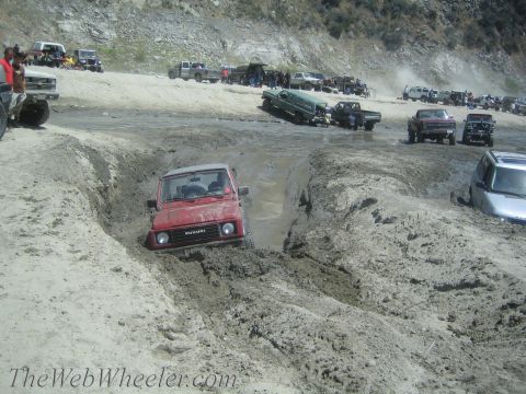 1987 Suzuki Samurai - A group of off-road vehicles navigate a challenging muddy terrain, with one Suzuki Samurai prominently stuck.