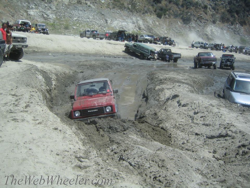 Red 1987 Suzuki Samurai stuck in a muddy ditch with other vehicles in the background