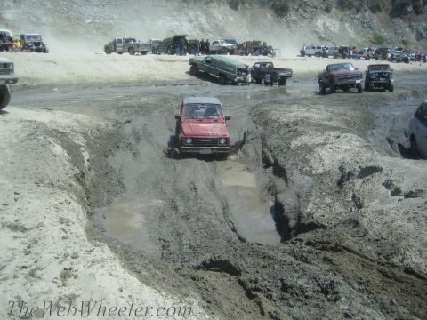 1987 Suzuki Samurai - A red 1987 Suzuki Samurai tackles a challenging muddy obstacle during an off-road event.
