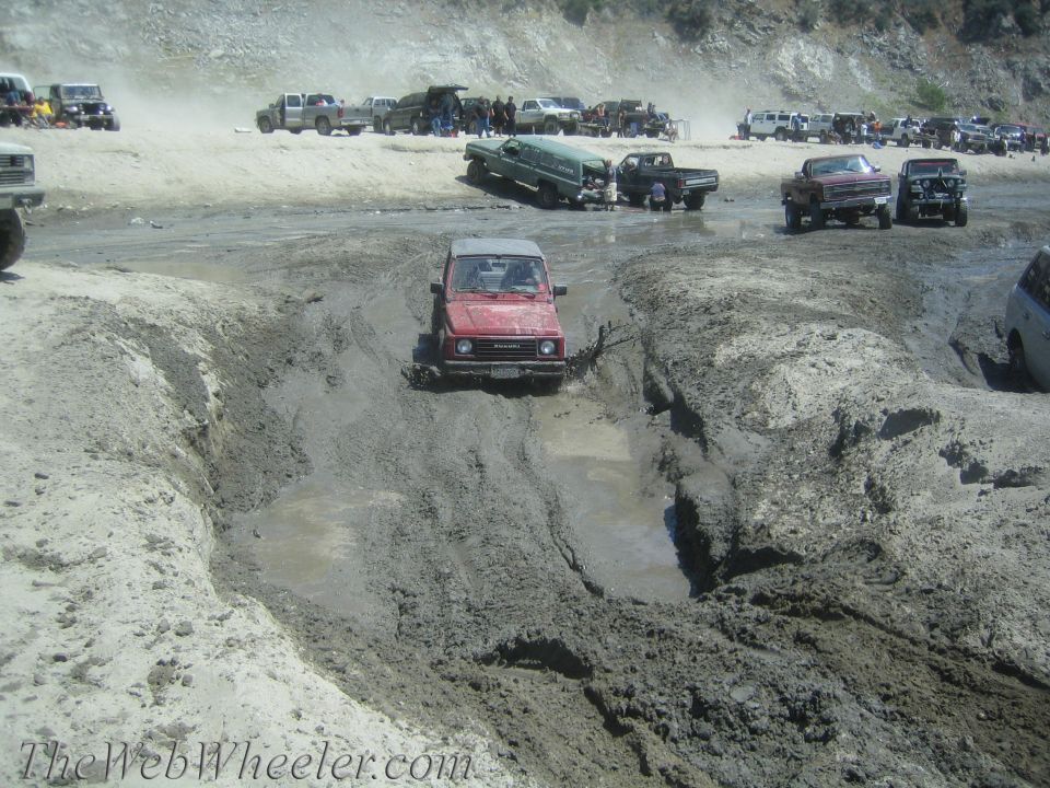 Red 1987 Suzuki Samurai driving through mud