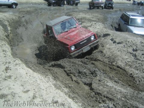 1987 Suzuki Samurai - Red Suzuki Samurai tackles a challenging mud obstacle during an off-road event.
