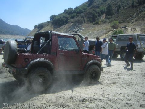 1987 Suzuki Samurai - A group of people and several off-road vehicles gather near a body of water on a sunny day.