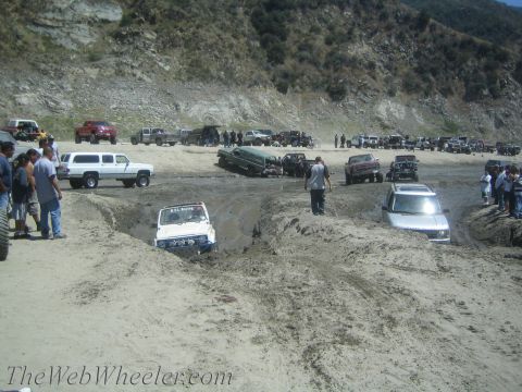 1987 Suzuki Samurai - Multiple off-road vehicles navigate a challenging mud course with spectators watching from the sidelines.