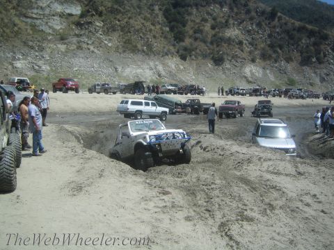 1987 Suzuki Samurai - A white 1987 Suzuki Samurai navigates a muddy off-road course, surrounded by spectators and other vehicles.