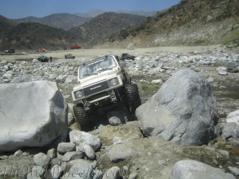 1987 Suzuki Samurai - A Suzuki Samurai tackles a challenging rocky path in a dry riverbed with mountains in the background.