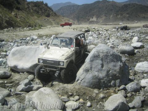 1987 Suzuki Samurai - This Suzuki Samurai is shown off-roading through a rocky terrain with mountains in the background.